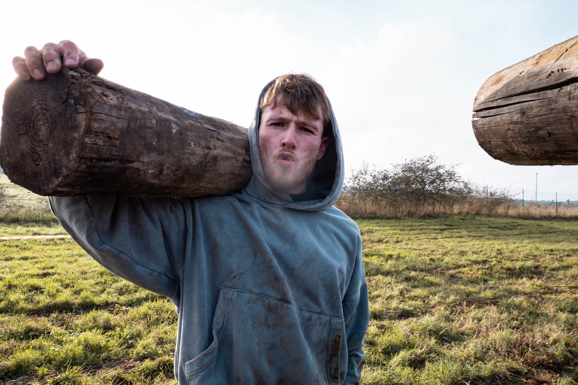 Un coureur d'OverBound portant un tronc d'arbre sur son épaule et regardant la caméra d'un air déterminé